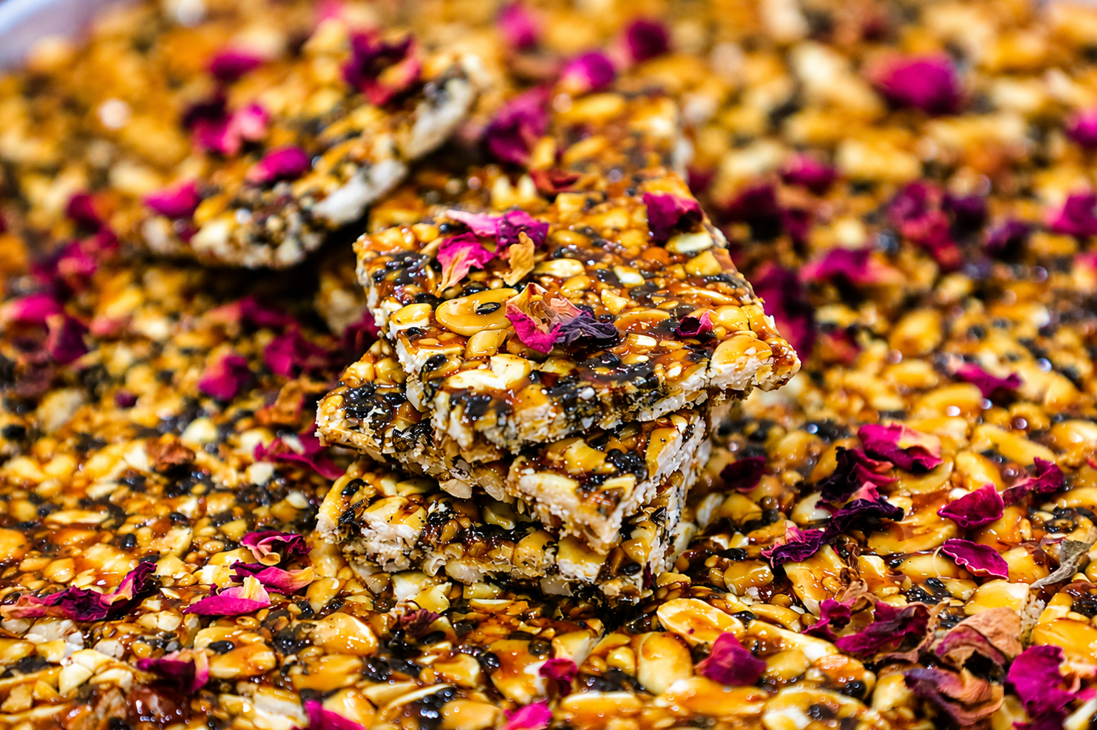 Chikki pieces on a brass plate with diya and dried flowers on a rustic wooden table